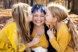 Three friends in matching yellow sweaters share a joyful moment while sitting together in a fall forest setting.