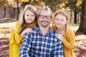 Family posing together outdoors amidst colorful fall leaves wearing coordinated blue and yellow outfits.