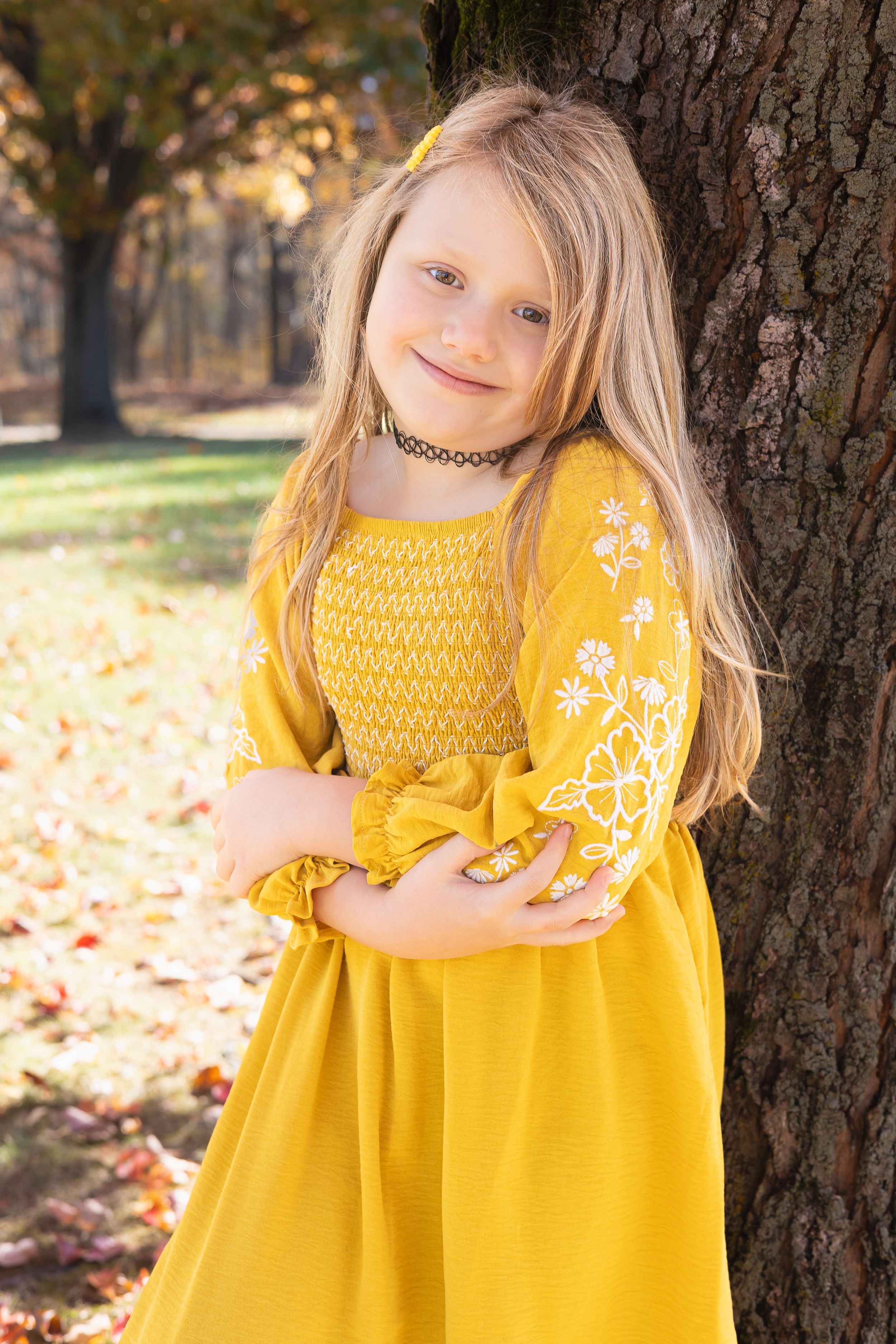 Yellow floral dress with embroidered sleeves photographed outdoors in autumn against a tree trunk.