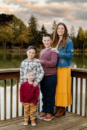 Family poses together on a wooden deck overlooking a serene lake at sunset with autumn trees in the background.