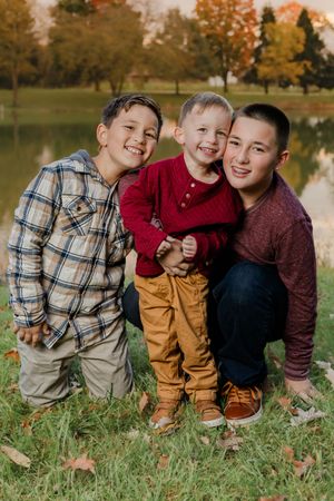 A candid series of fall outdoor photos shows three figures sitting together in grass near a lake with autumn trees.