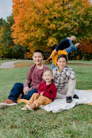 A family relaxes together on a picnic blanket surrounded by vibrant autumn foliage in a peaceful park setting.