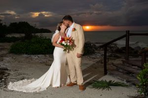 A couple shares a romantic moment at sunset on a beach boardwalk with dramatic orange clouds in the background.