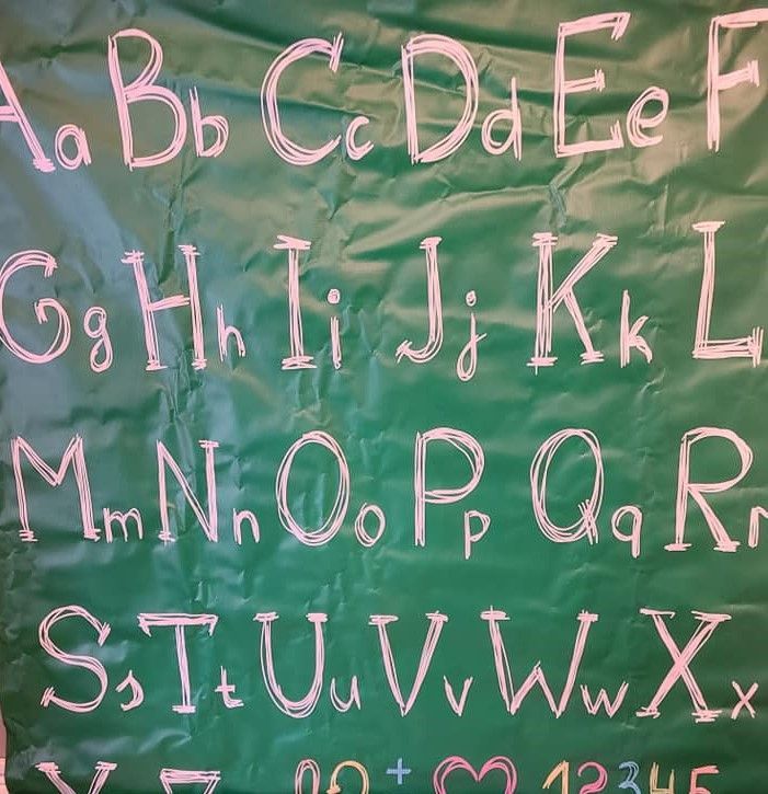 Handwritten alphabet letters A through X displayed on green chalkboard backdrop.