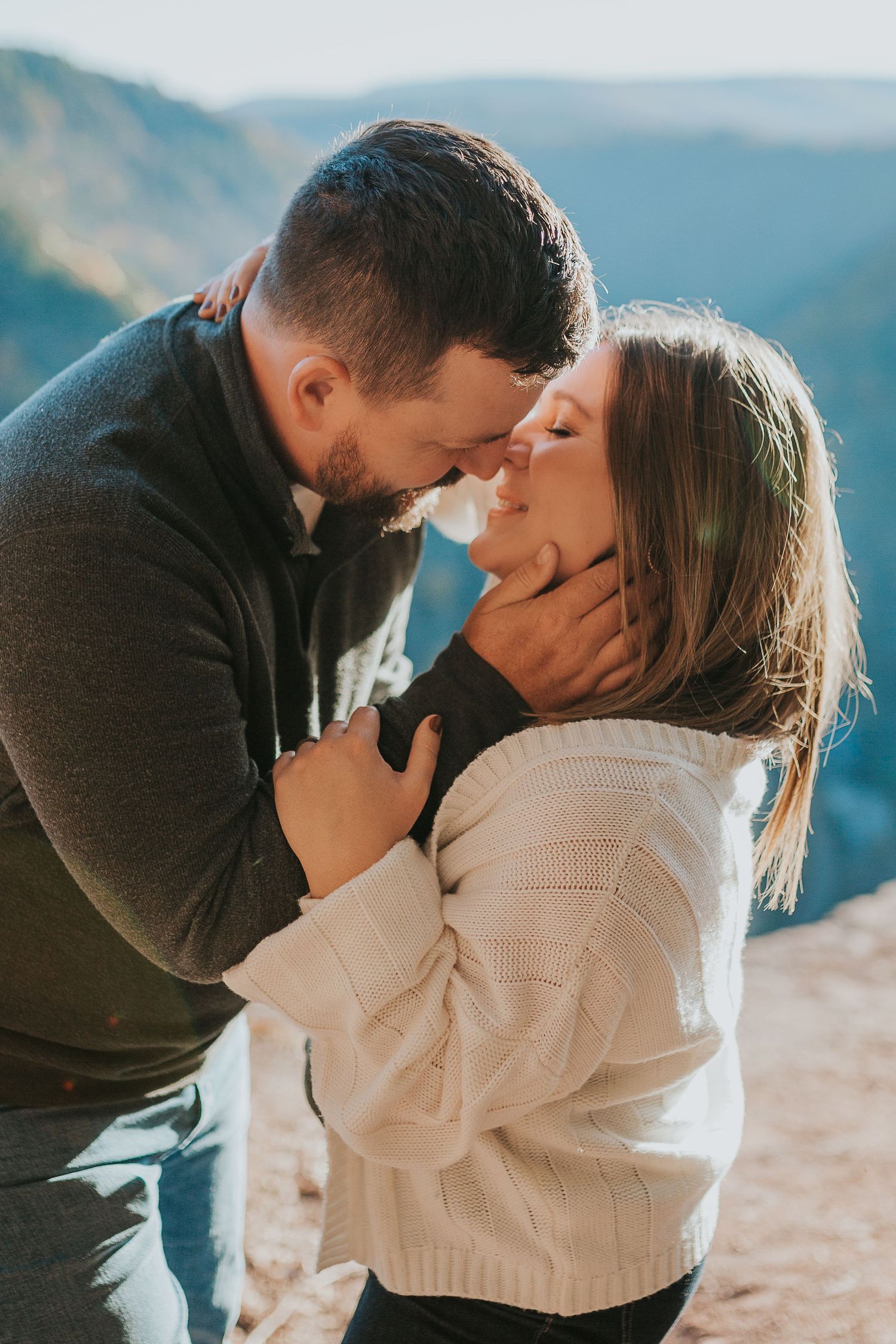 Romantic couple embracing on mountain cliff during golden hour wearing cozy sweaters.