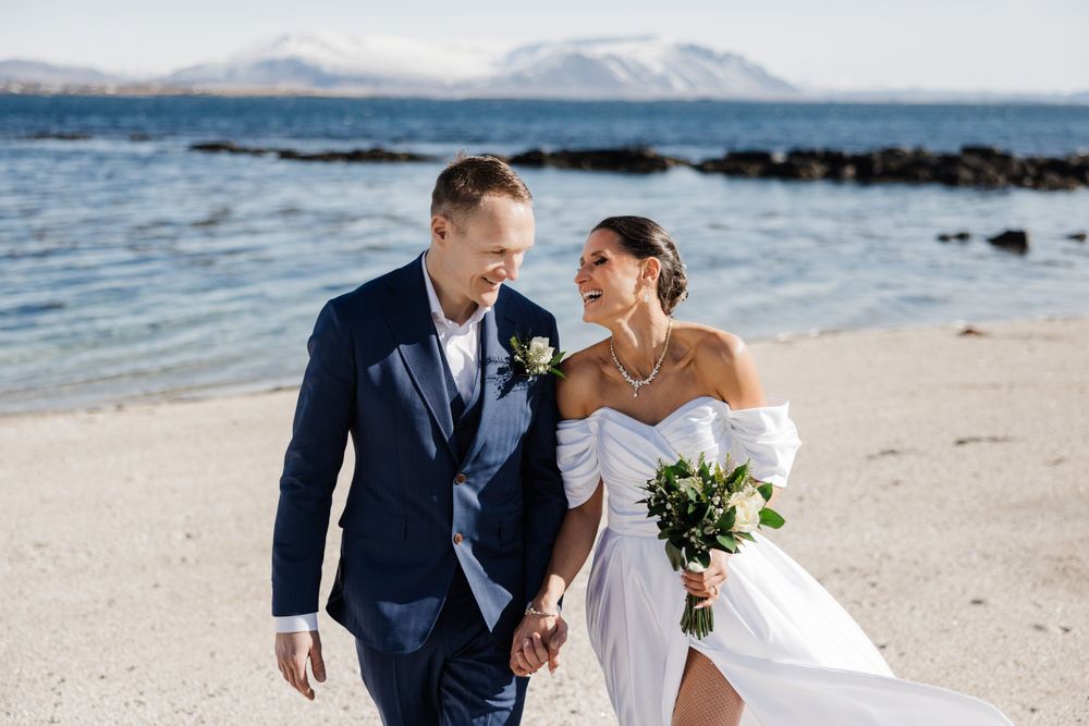 A couple shares a moment on a beach with mountains and rocky coastline.