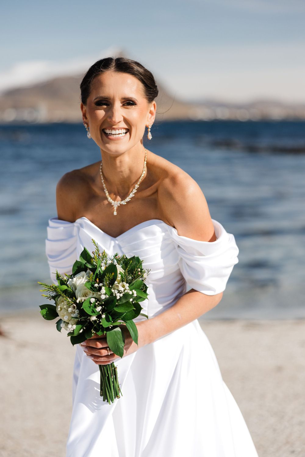 Beautiful bridal portrait on beach with mountains and ocean in background.