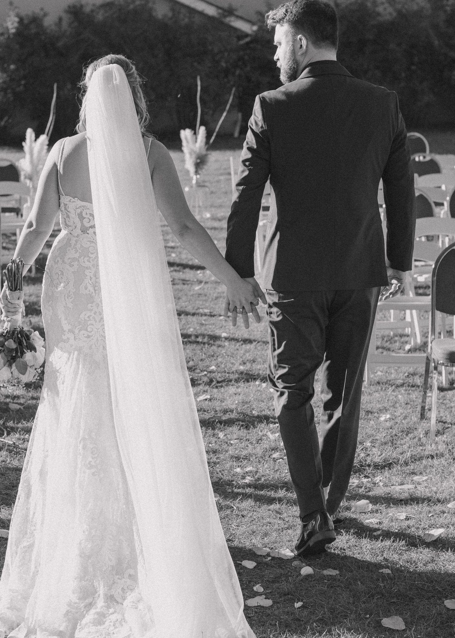 Back view of bride and groom walking down the aisle in a black and white photo, capturing a timeless wedding moment.