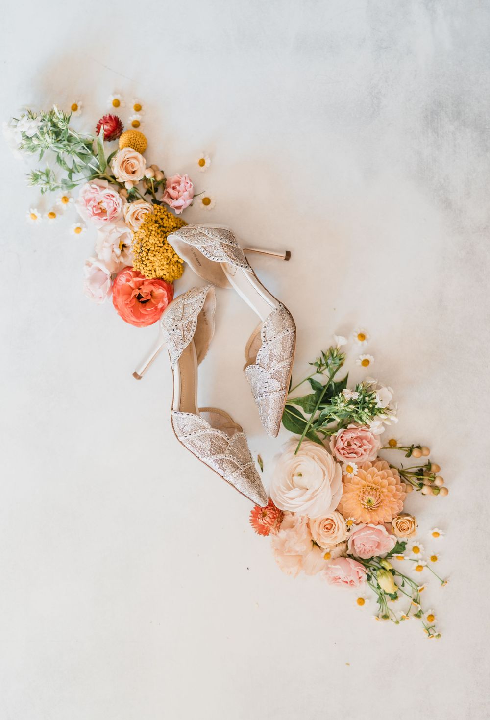 Flat lay of White lace wedding heels with coral and peach flowers, berries and greenery on a light background by VT wedding photographer