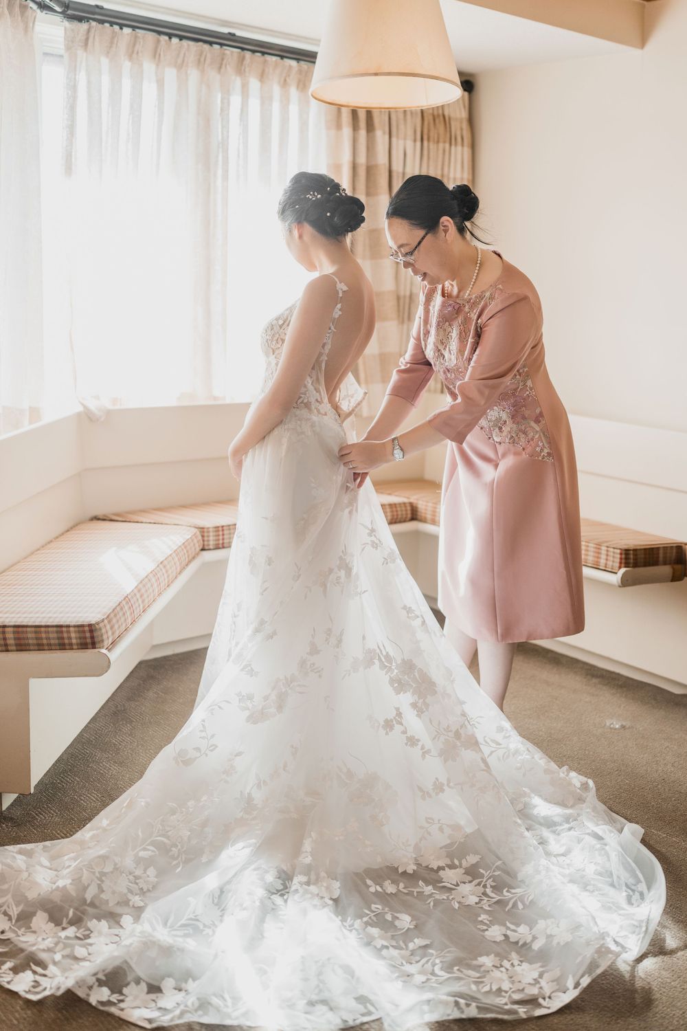 Woman helps bride with wedding dressin a sunlit room at Trapp Family Lodge, a Vermont wedding venue. in Stowe, VT