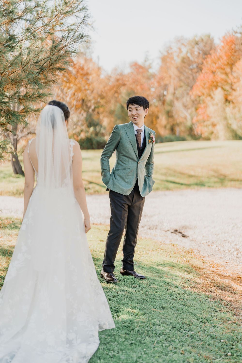 A groom in green tux jacket sees bride and reacts emotionally during autumn wedding with fall foliage in photo by Maine wedding photographer