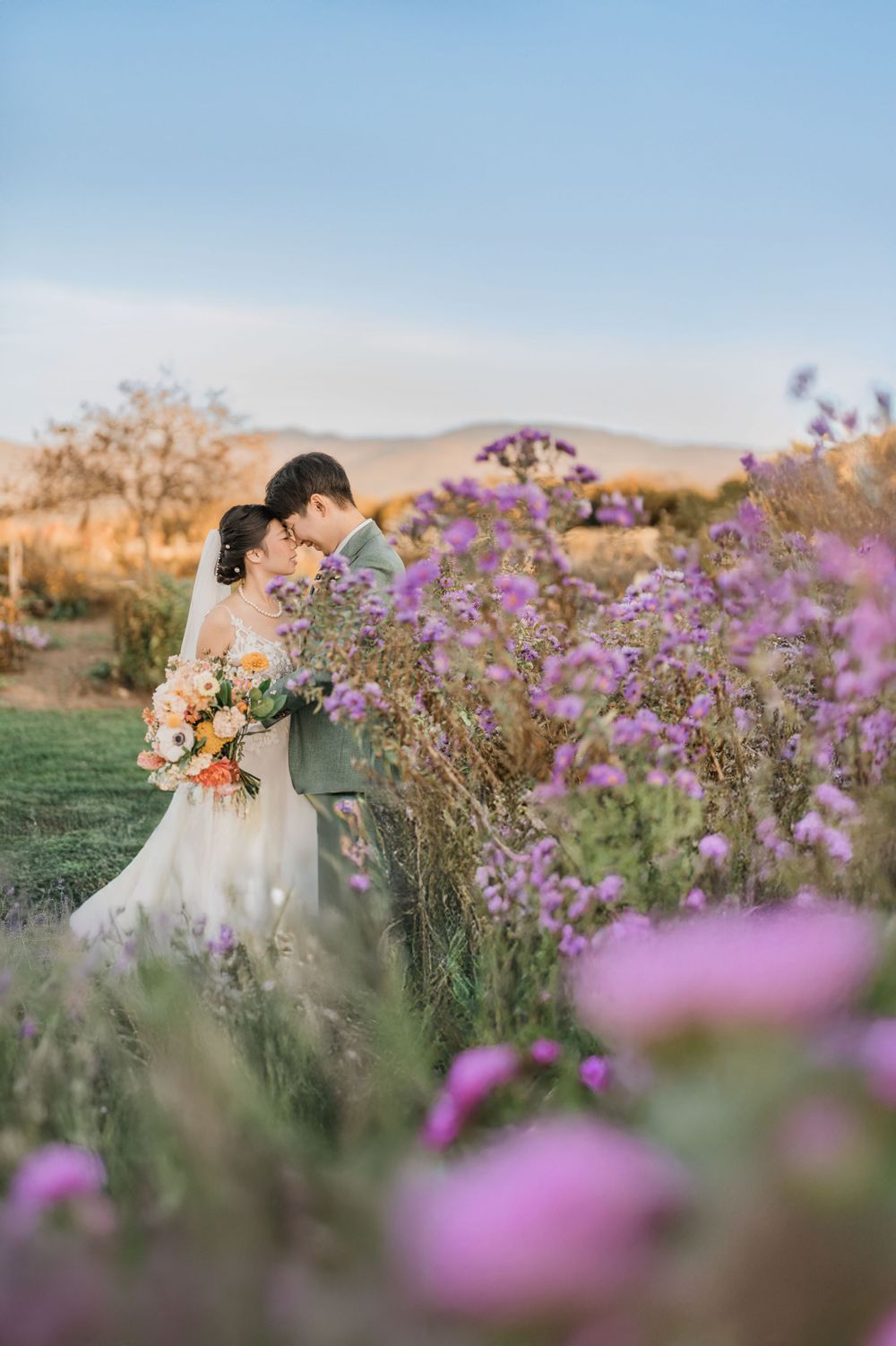 A bride and groom embrace among purple wildflowers during a sunset wedding photoshoot in a meadow at historic Vermont wedding venue