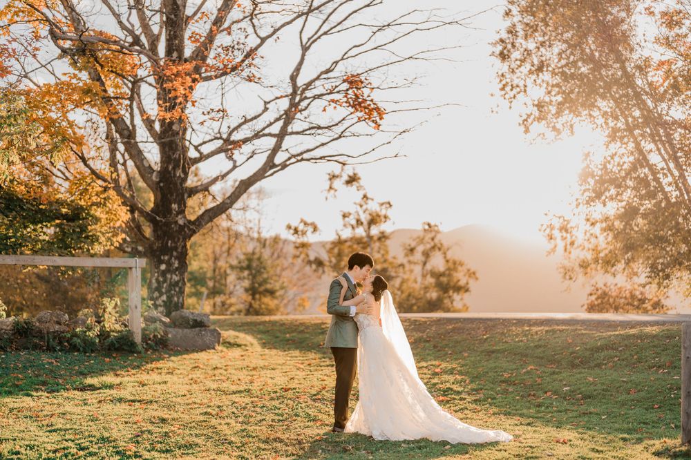 A couple embraces during sunset during outdoor autumn wedding photos with fall leaves in the background by Maine wedding photographer
