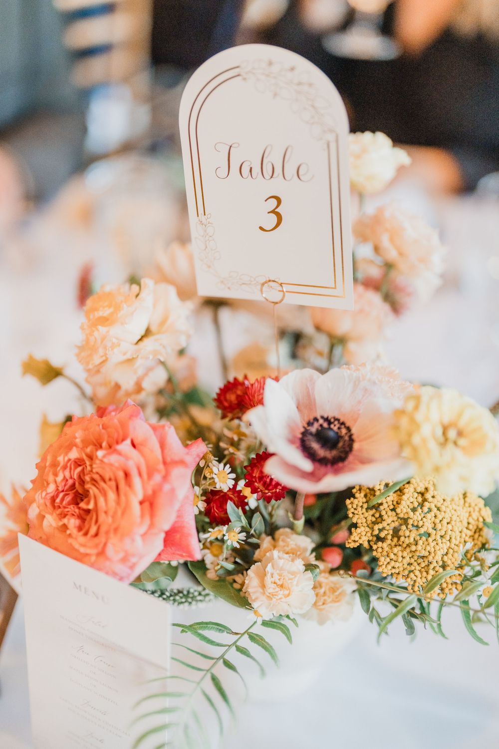 Elegant wedding table number card displayed amongst coral, peach and white fall floral centerpiece arrangement at Trapp Family Lodge