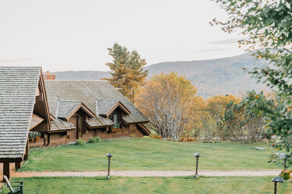 Rustic wooden lodge buildings nestled on a grassy hillside with autumn mountains in the background at Trapp Family Lodge in Stowe, Vermont
