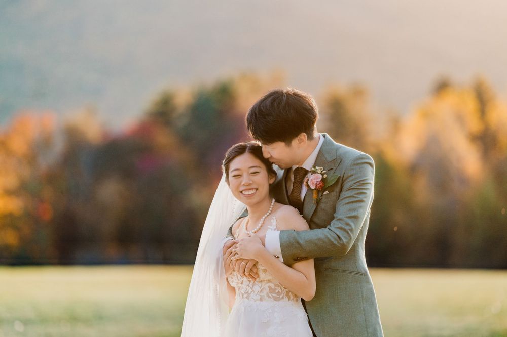 A joyful couple embraces in a golden autumn meadow during their wedding photoshoot at Trapp Family Lodge in Stowe by vt wedding photographer