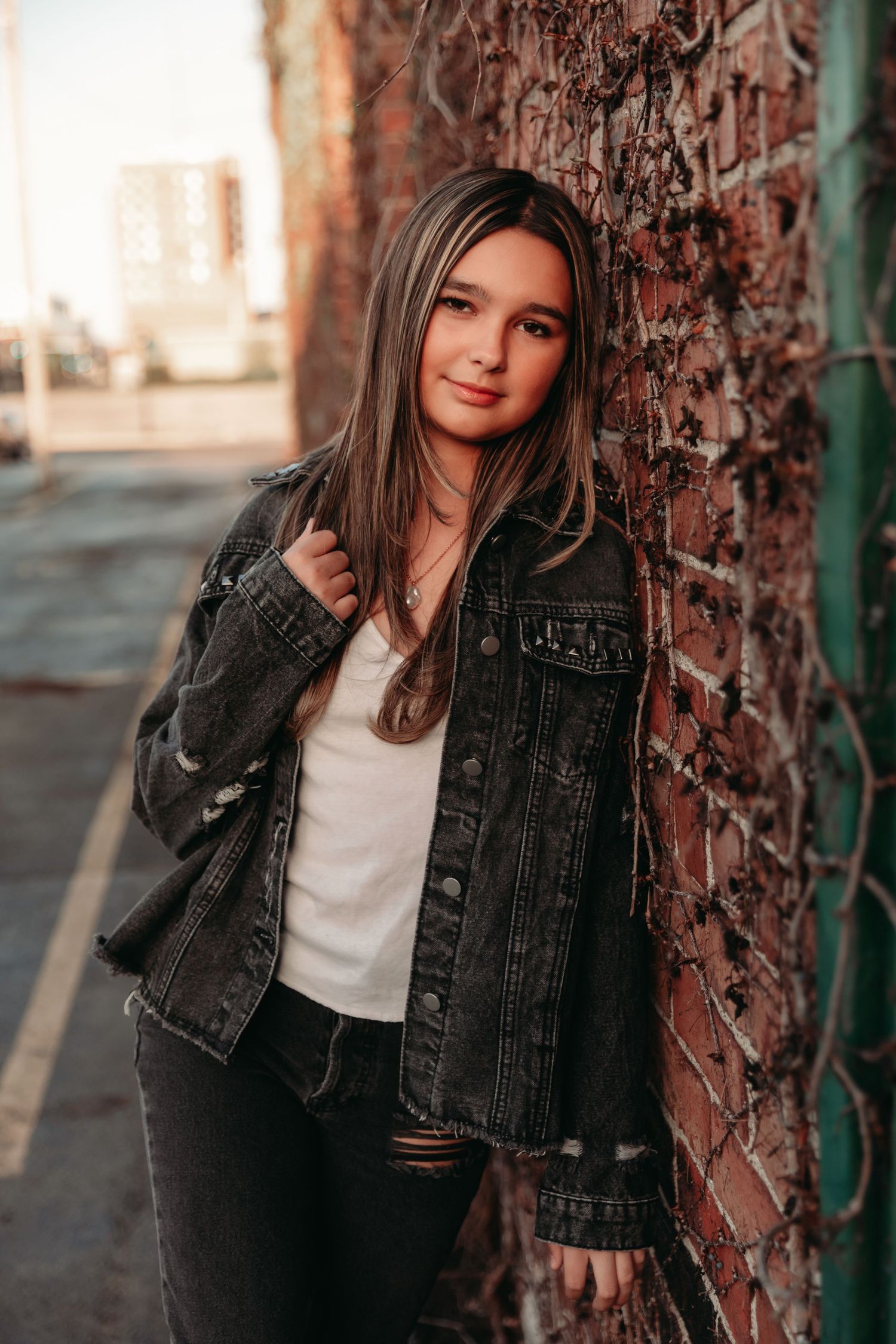 Urban fashion portrait in denim jacket against brick wall during sunset.