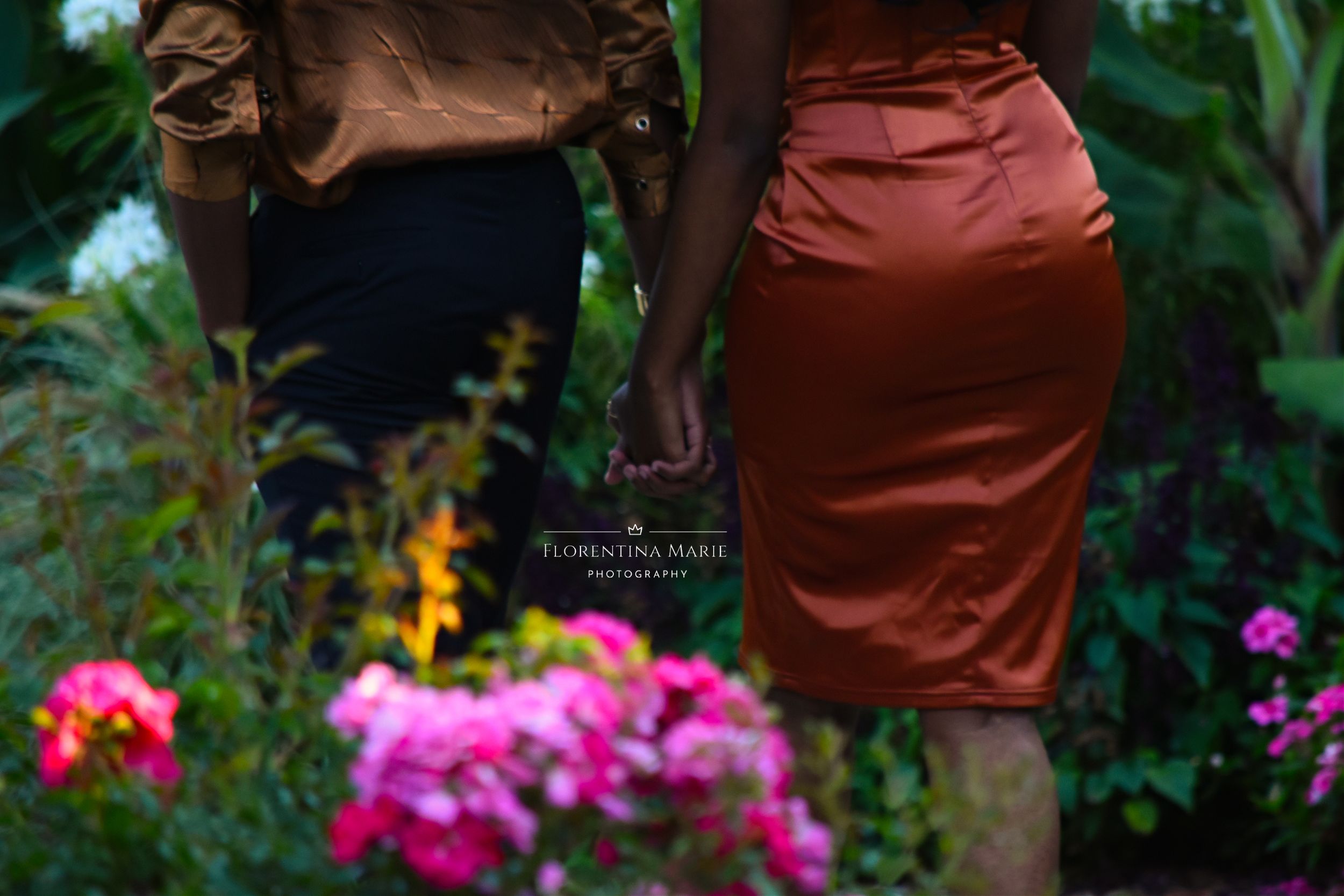 Close-up of two people in formal attire standing among colorful garden flowers.