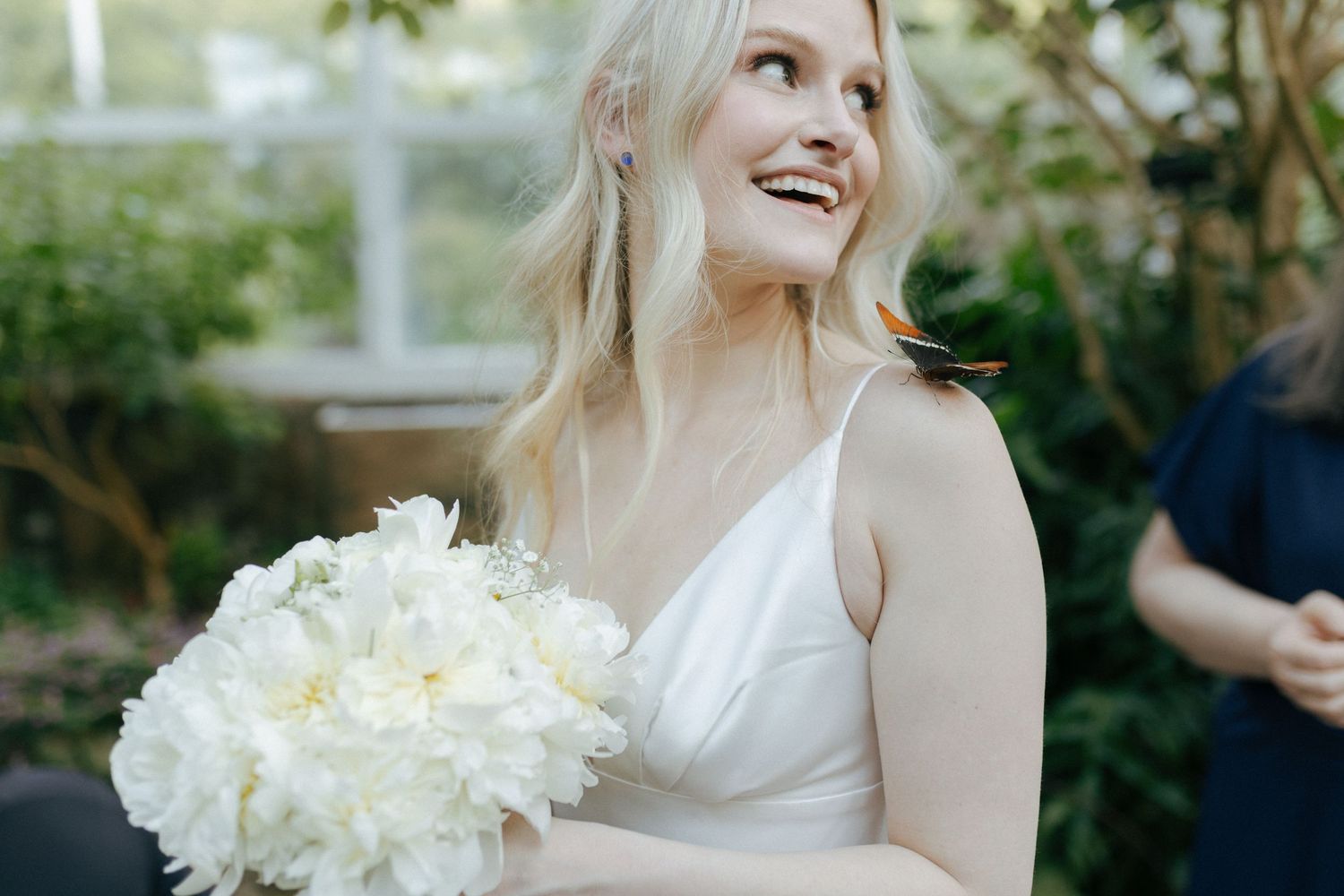 A joyful person in a white dress holding a bouquet of white flowers in an outdoor garden setting.