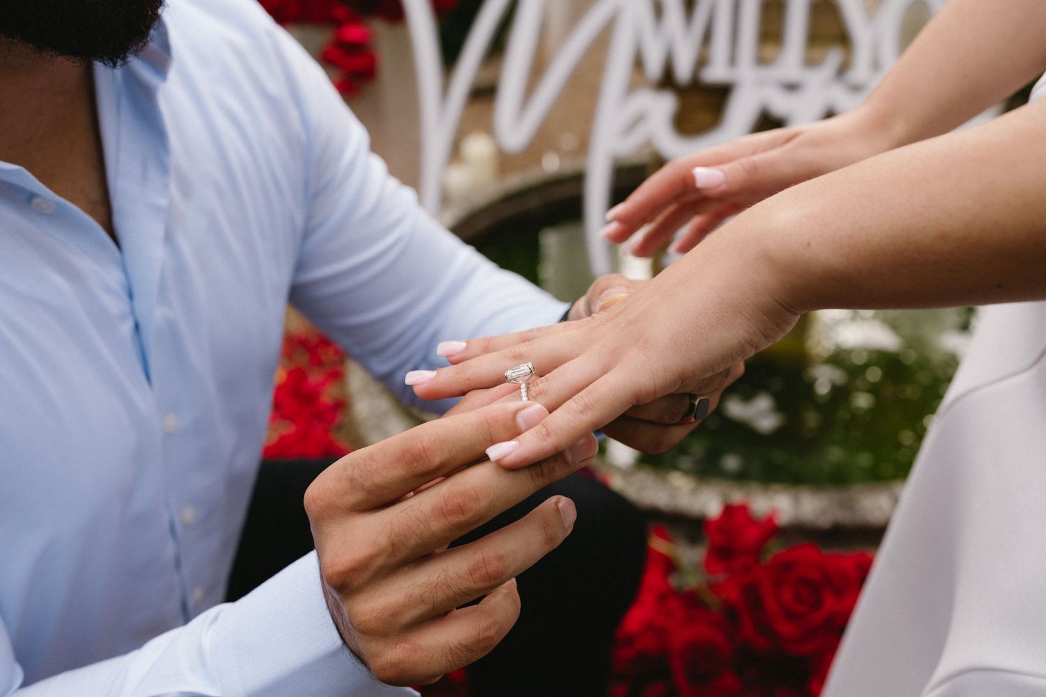 Close-up shot of hands during proposal moment as ring is being placed on finger in garden setting.