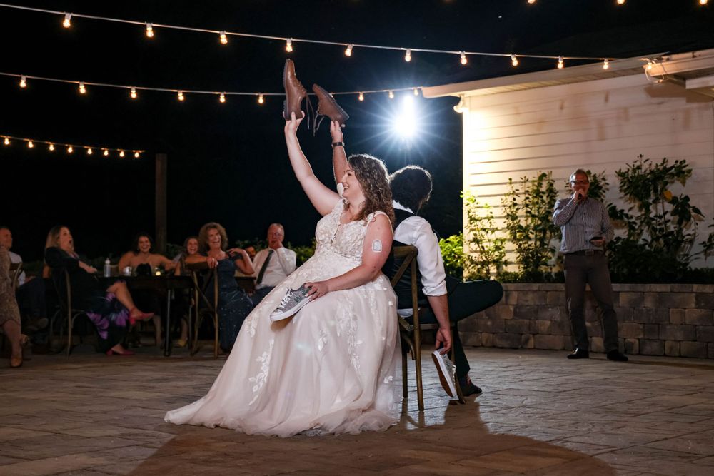 A couple performs a playful dance move during their wedding reception under string lights on an outdoor patio.