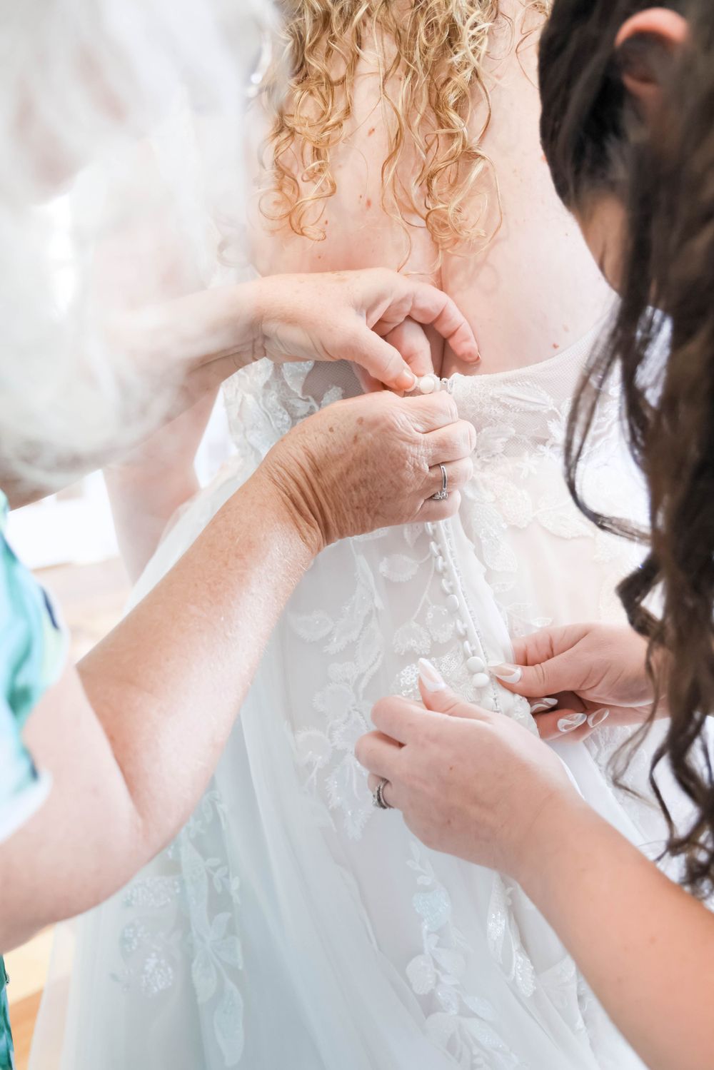 Hands carefully adjusting the intricate lace details of a white wedding dress during final preparations.