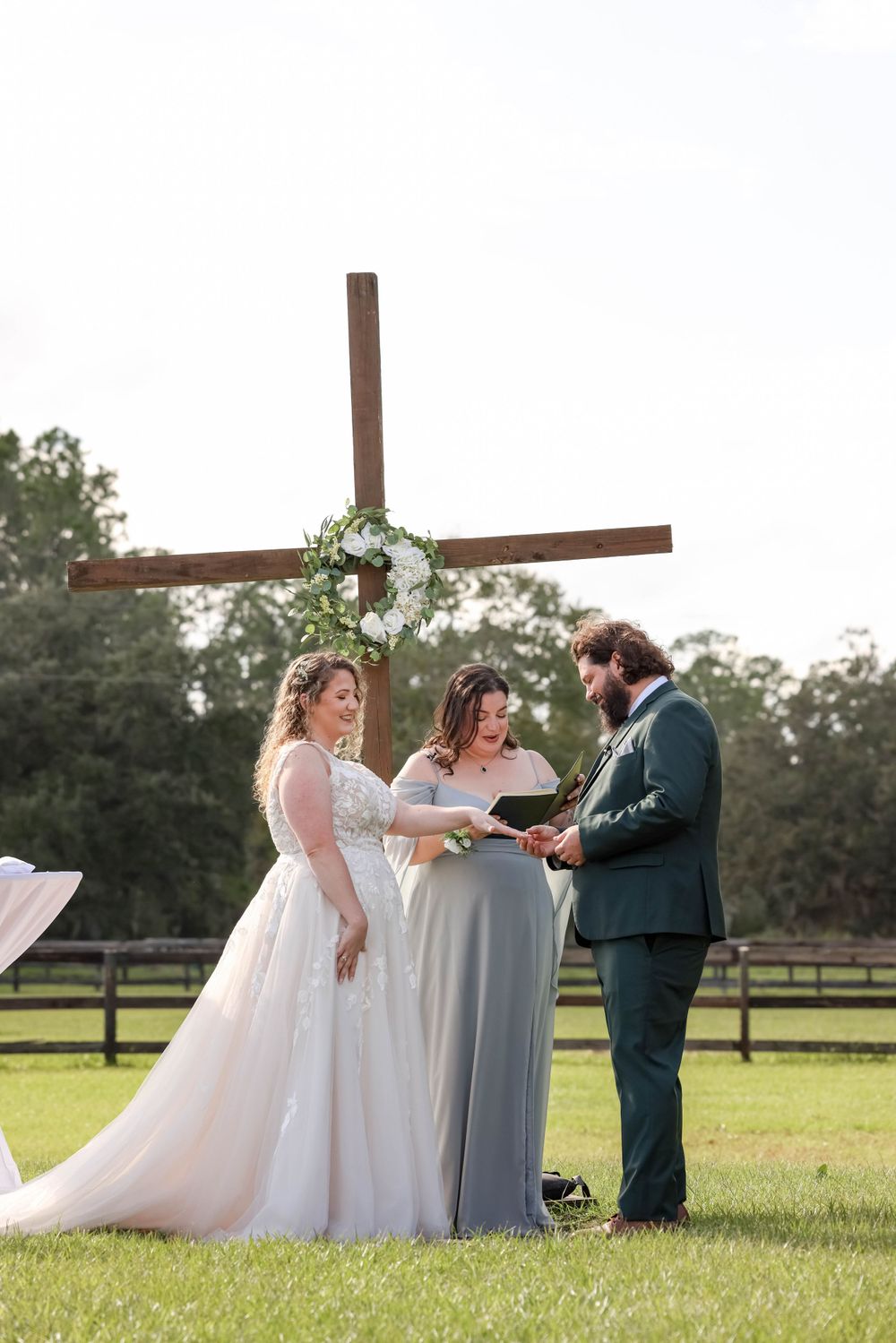 An outdoor wedding ceremony taking place under a wooden cross decorated with flowers.