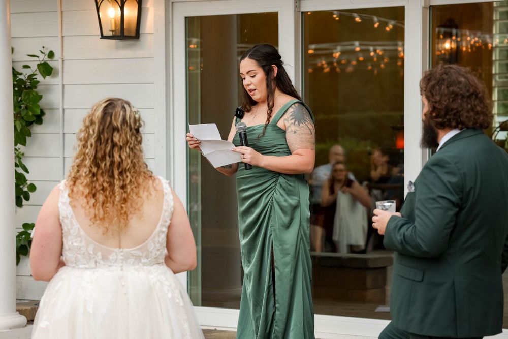 Wedding guests share toasts during an outdoor reception by a white house with string lights.