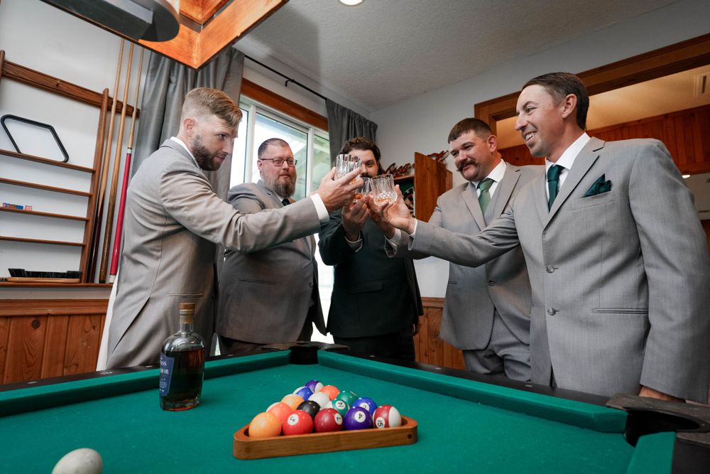 Wedding party members enjoy a game of pool in formal attire.