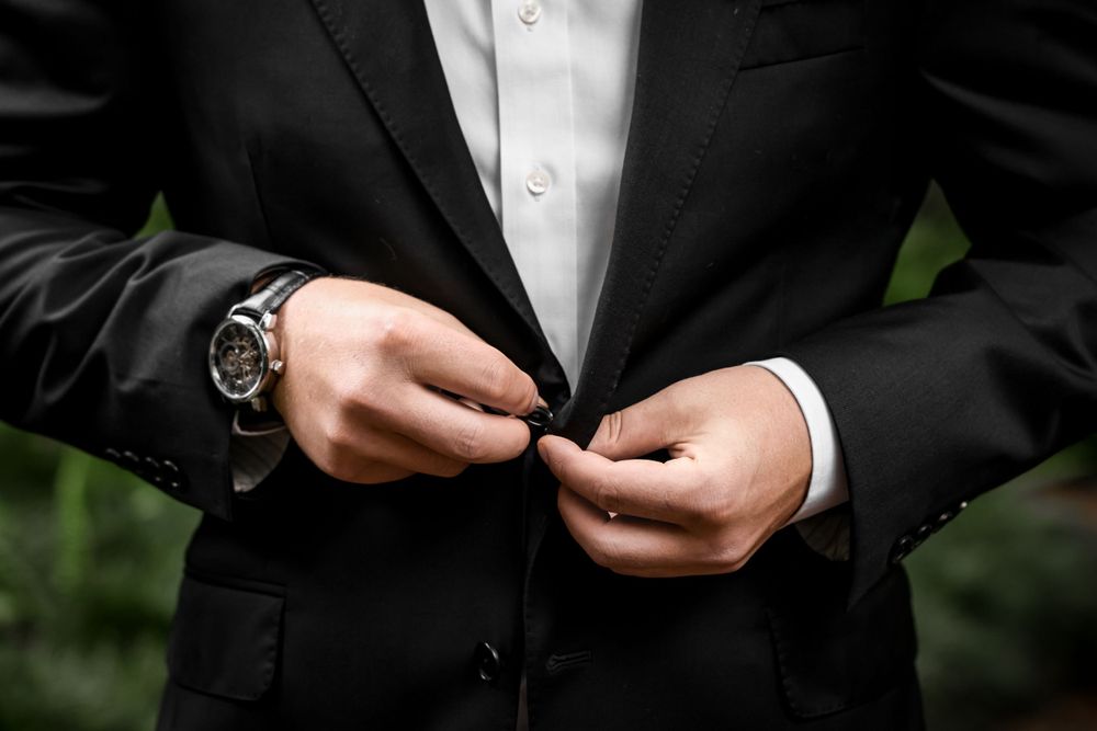 Close-up of hands buttoning a formal black suit jacket with luxury watch.
