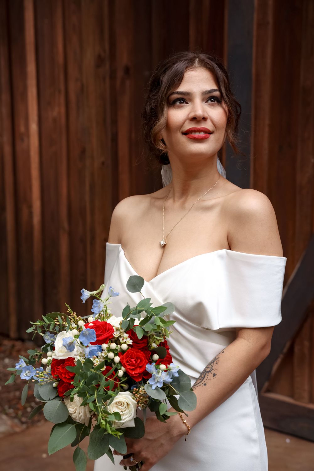 Elegant off-shoulder white wedding dress with red and blue floral bouquet.