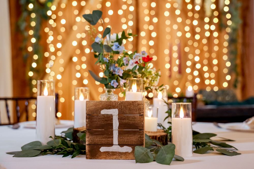 Rustic wedding table decor with wooden number one, white candles and fairy lights backdrop.