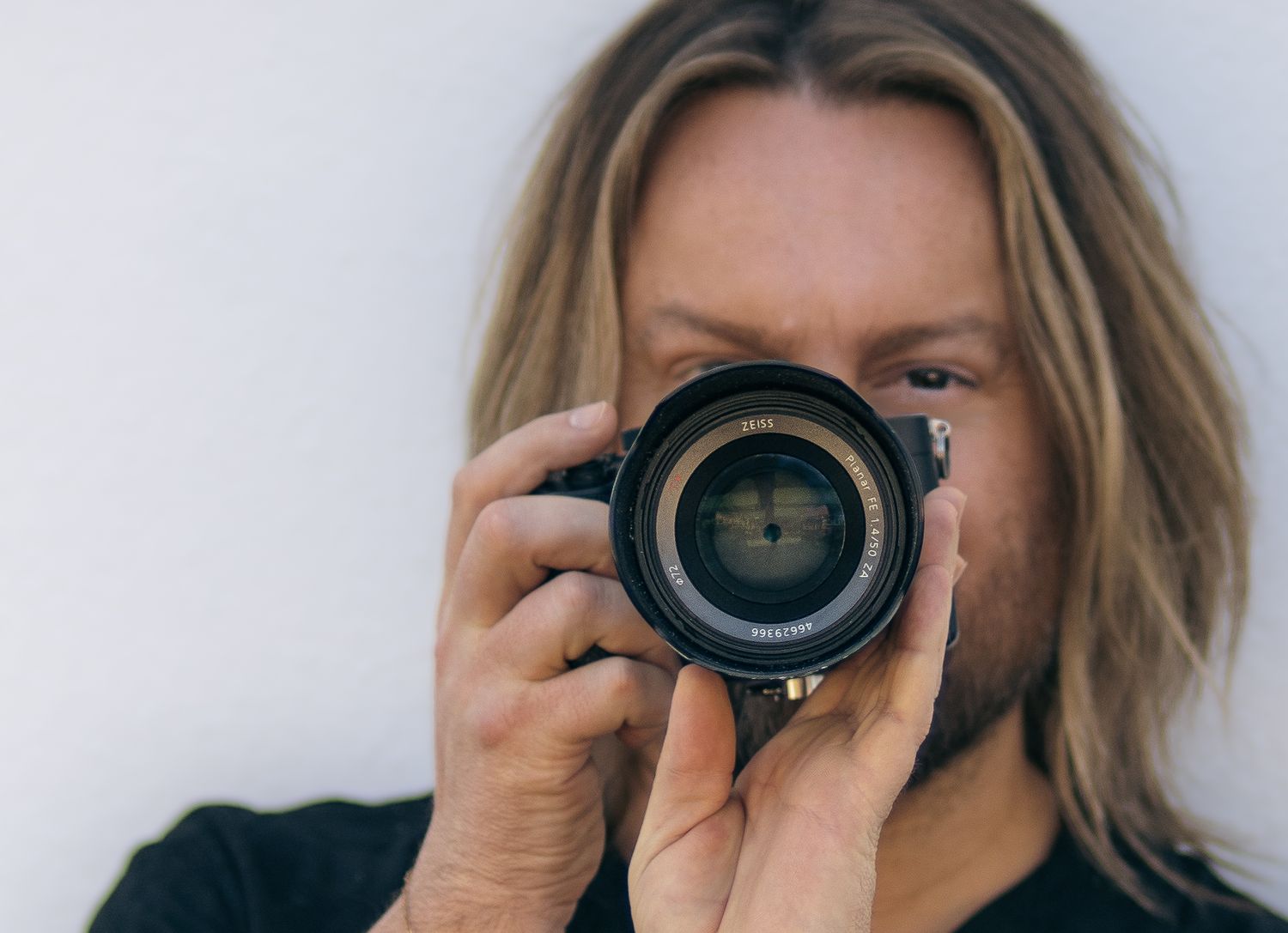 A photographer holding a professional camera with a large lens in front of their face.