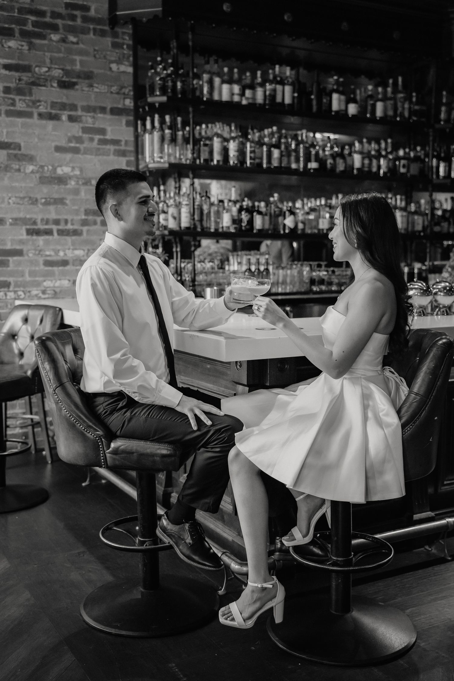 A couple shares an intimate moment at a rustic bar with exposed brick walls and shelves of liquor bottles.