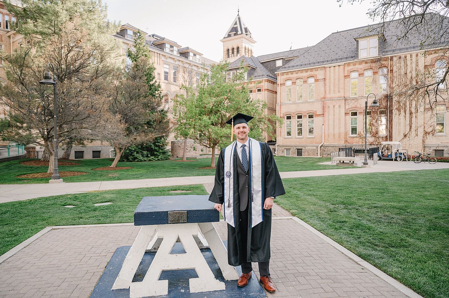 A graduate in cap and gown stands on a collegiate path with Auburn University buildings in the background.