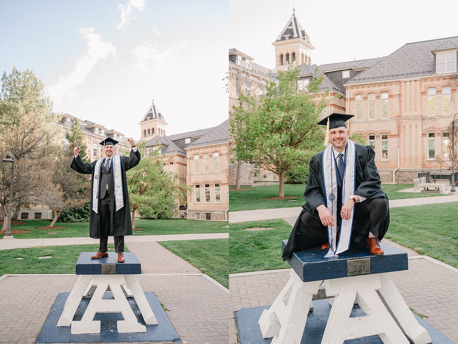 Graduate stands triumphantly on large university letters on campus lawn with historic brick buildings in background.