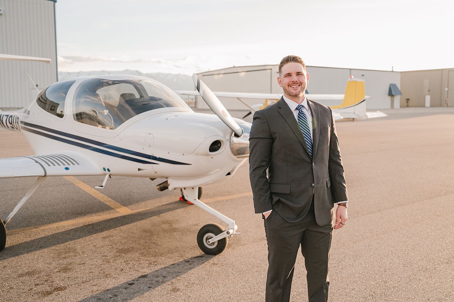 A small private aircraft parked on an airfield with someone in business attire standing beside it.