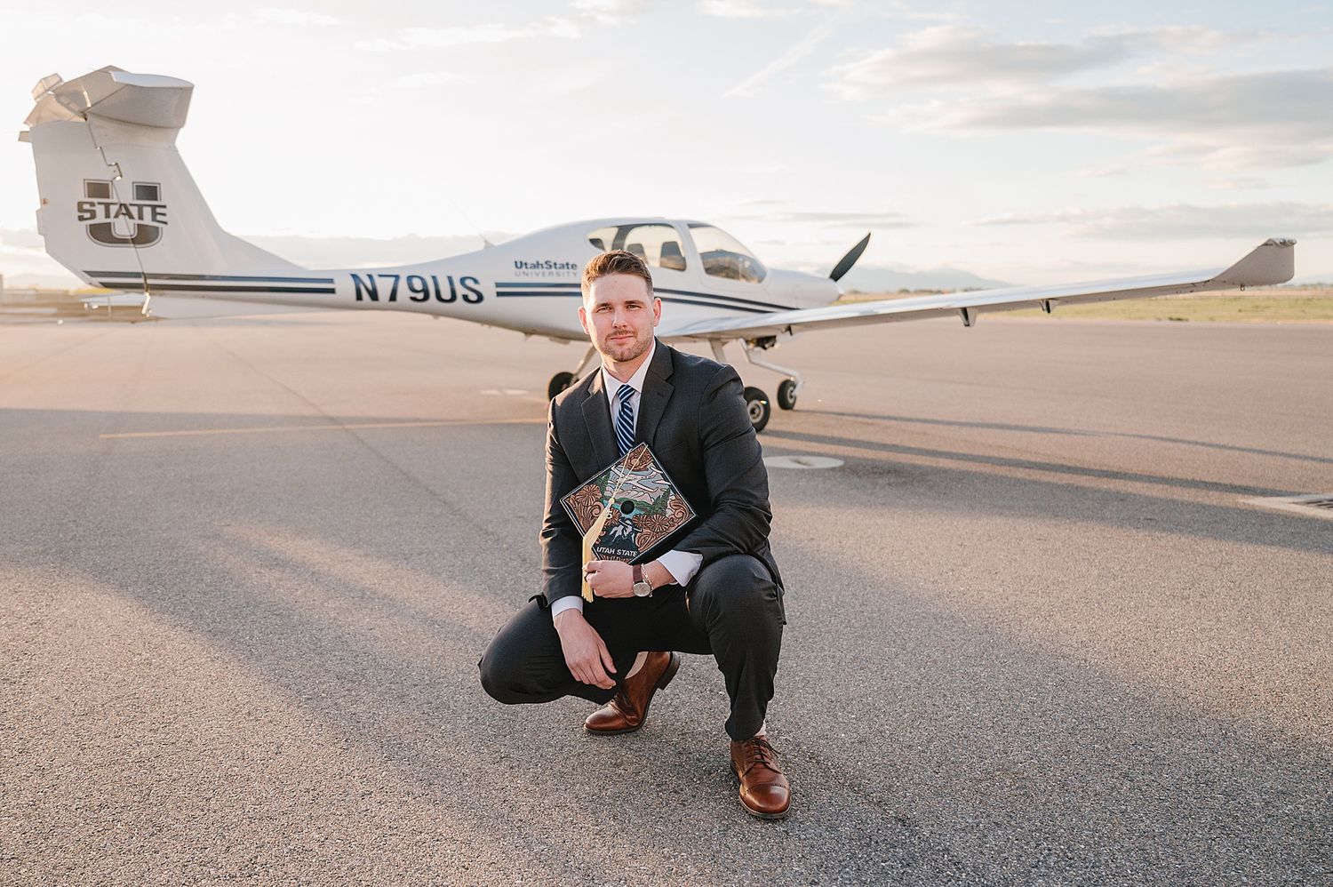 A small private aircraft is parked on the tarmac at an airport during sunset as someone poses with their dog.