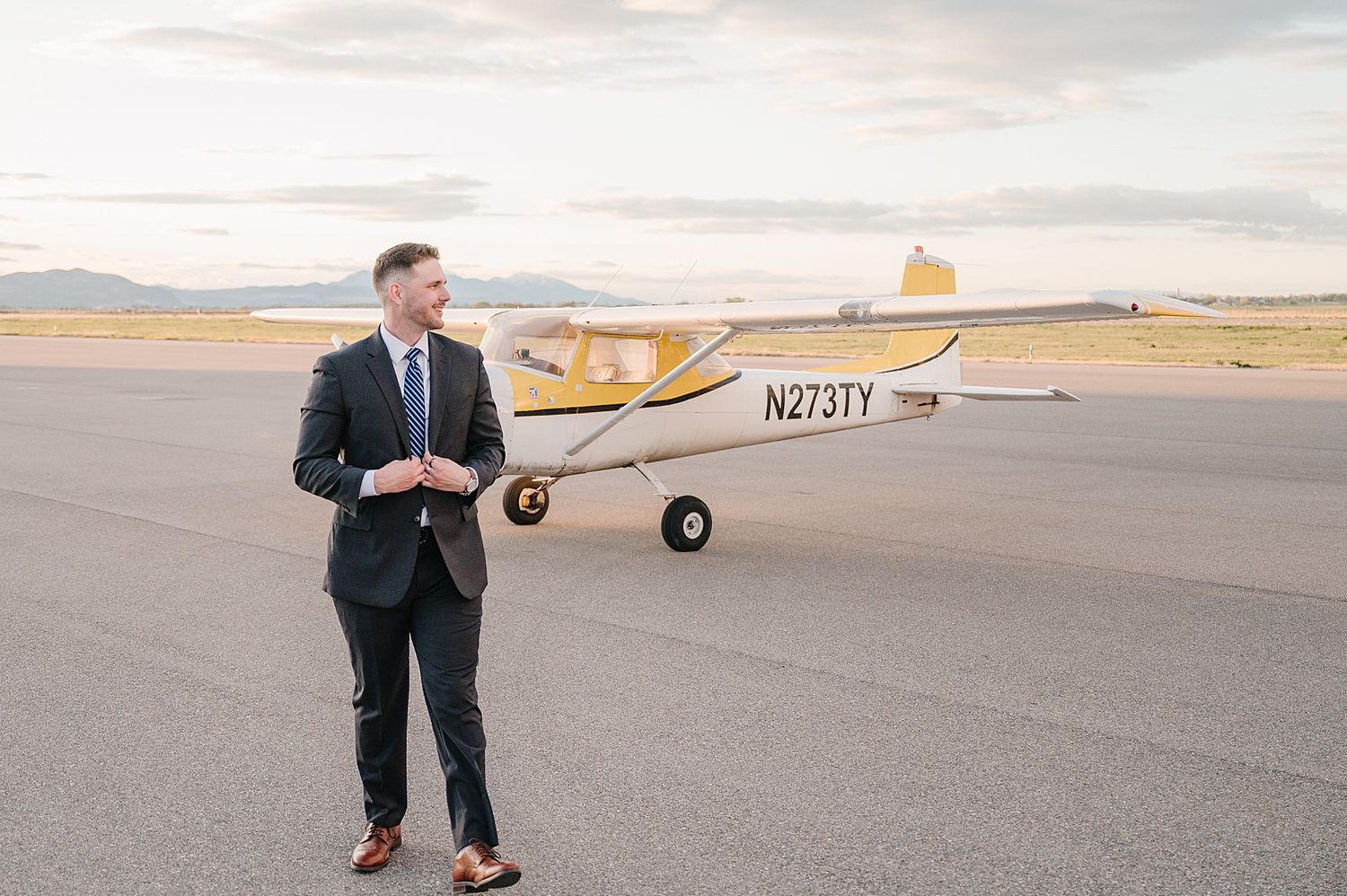 A small yellow Cessna aircraft parked on an airport tarmac at dusk with mountains visible in the background.