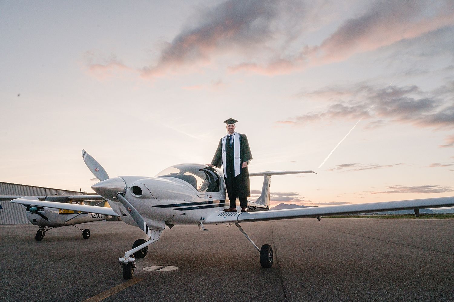 A small private aircraft parked on tarmac during sunset with a silhouette standing on top of the fuselage.