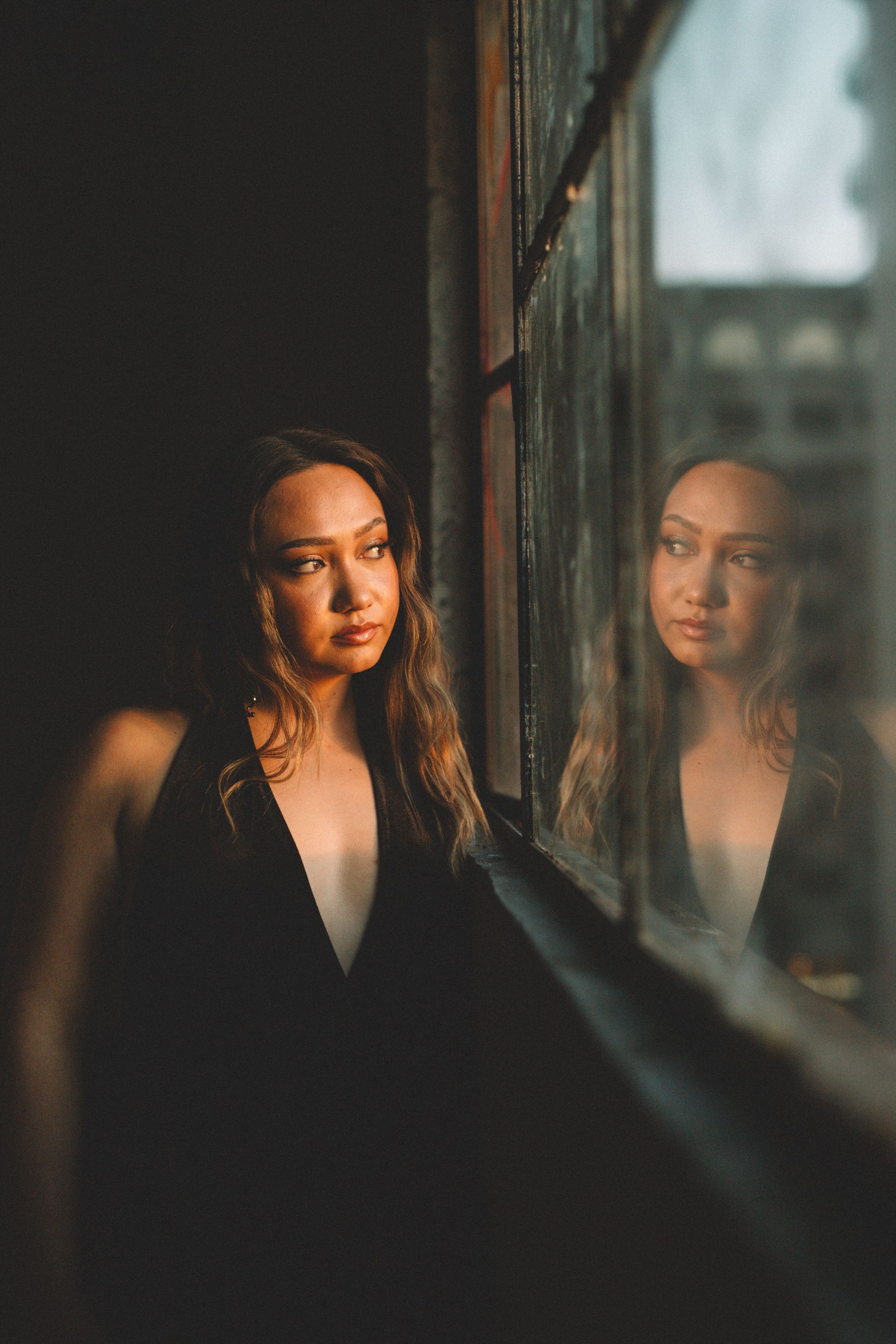 An artistic portrait against a window showing a reflection in dramatic low-key lighting.