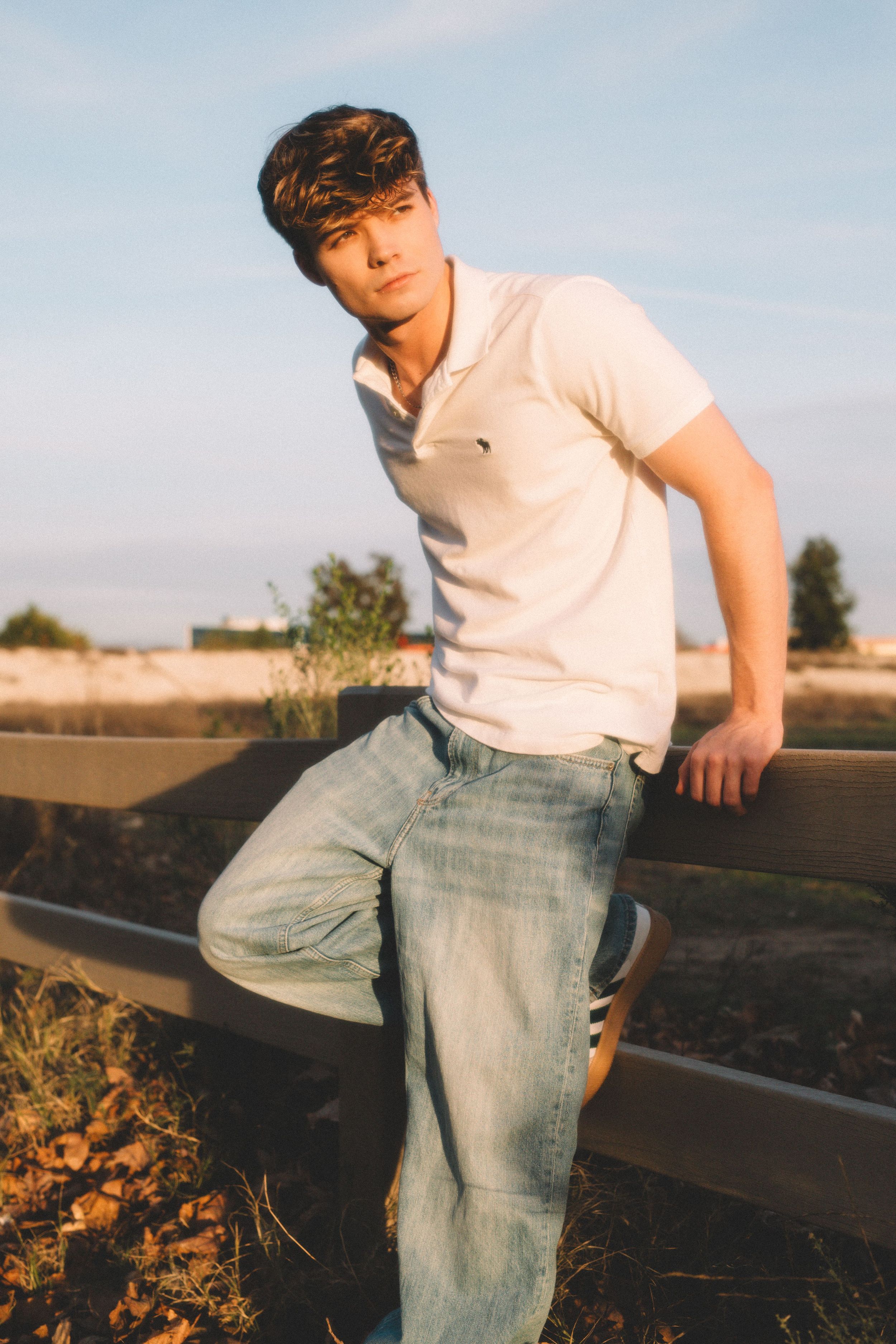 Person in white polo leans against wooden railing during golden hour.