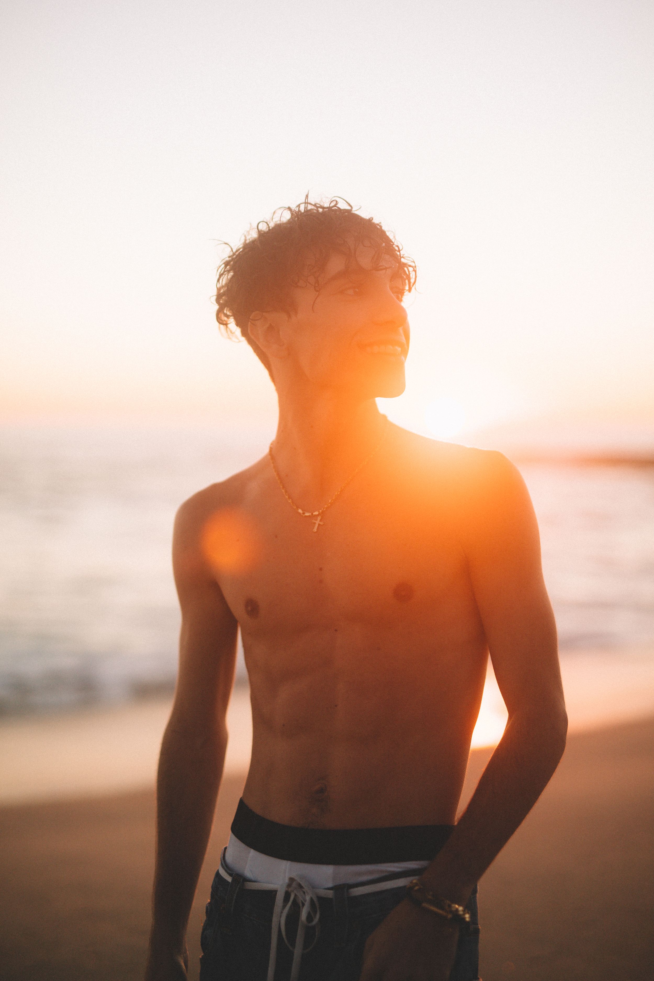 Silhouette of person with curly hair backlit by golden sunset at beach.