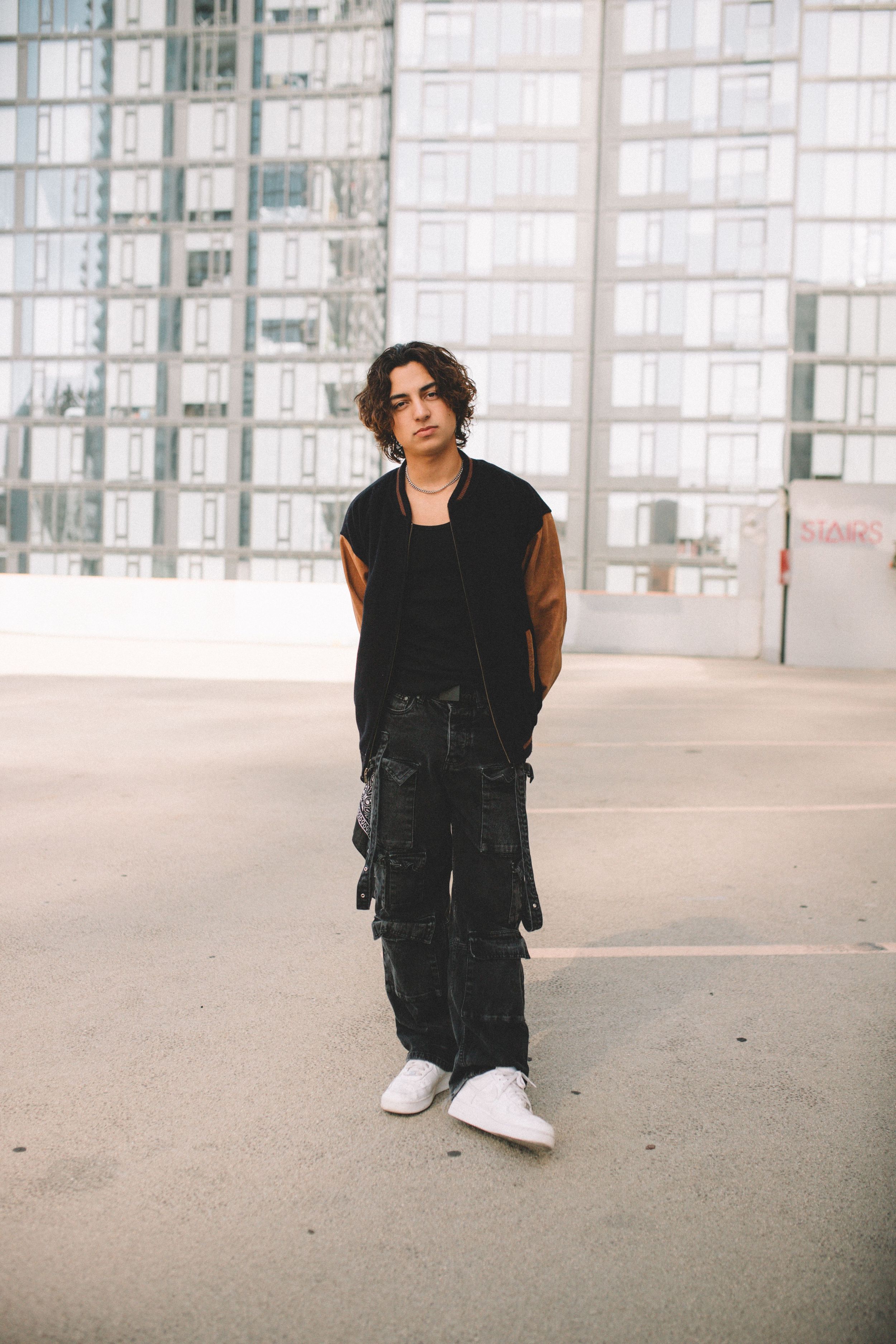Person wearing black vest and cargo pants poses in front of modern glass building.