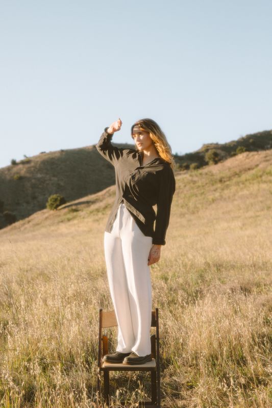 A fashion portrait of someone standing on a wooden stool in a mountain field.