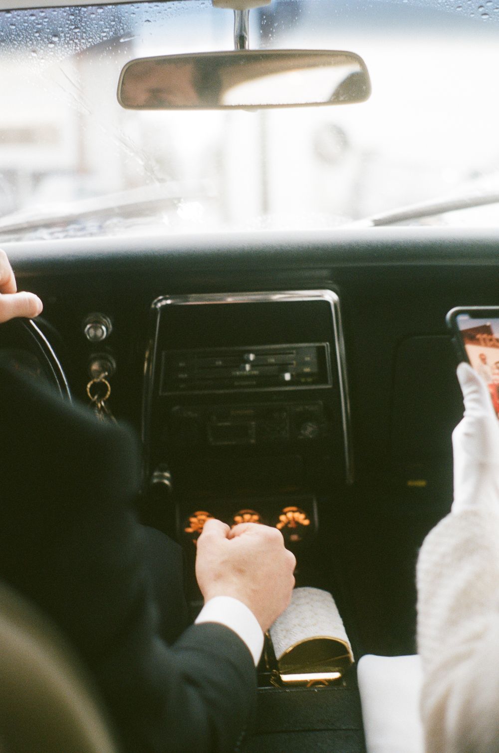 Interior view of a car dashboard through a rainy windshield.