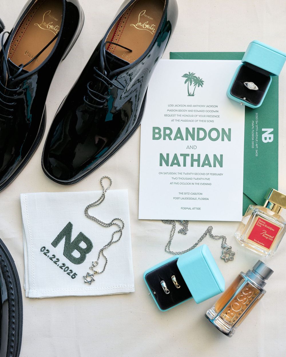 Wedding details flatlay with black dress shoes, invitation, rings, and perfume.