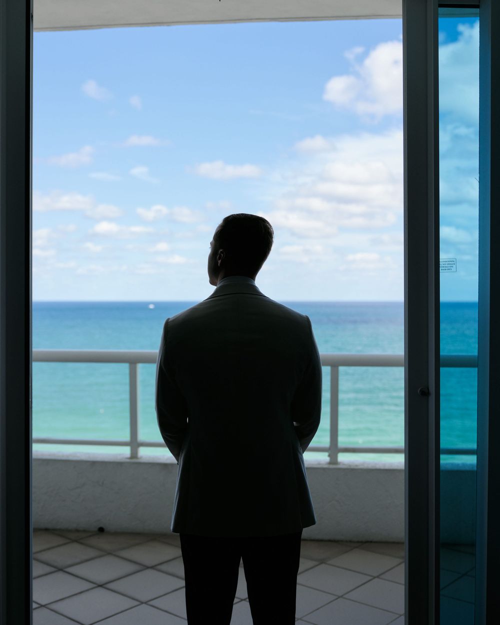Silhouette of a person in a suit looking out over the ocean from a balcony.