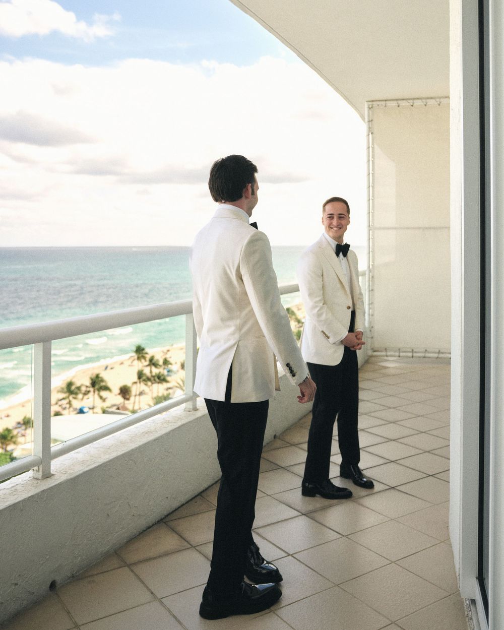 Two people in white dinner jackets standing on oceanfront balcony during formal event.