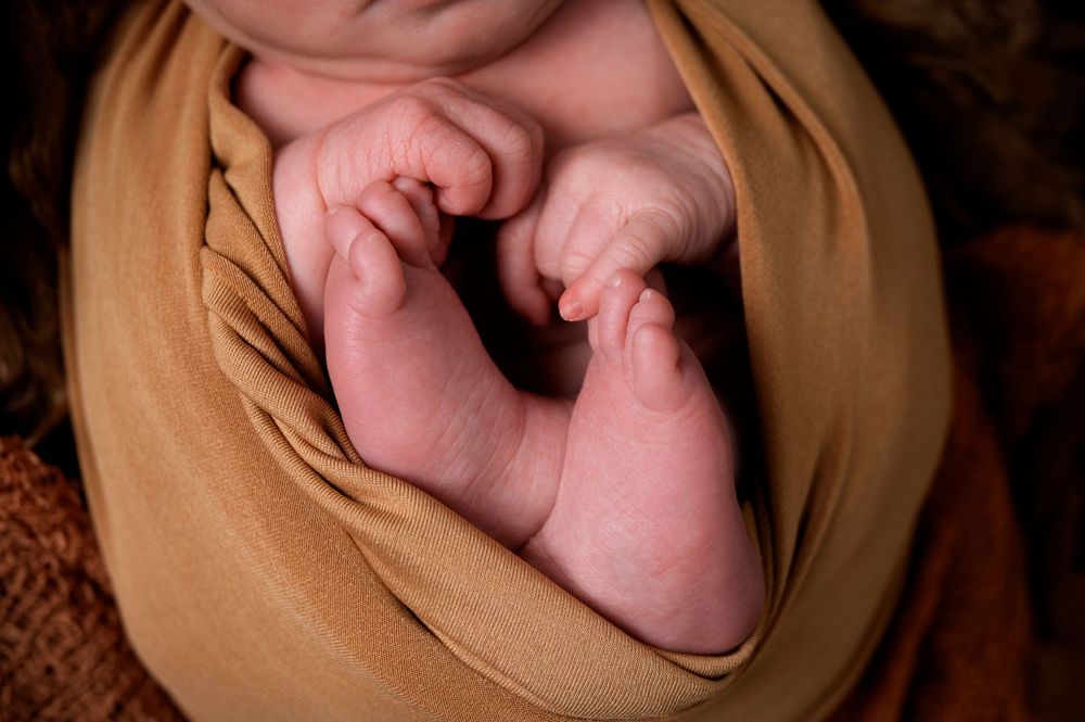 Close-up of tiny newborn feet wrapped in tan fabric.